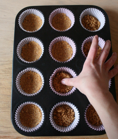 muffin tin with graham cracker crusts inside of paper cupcake holders 