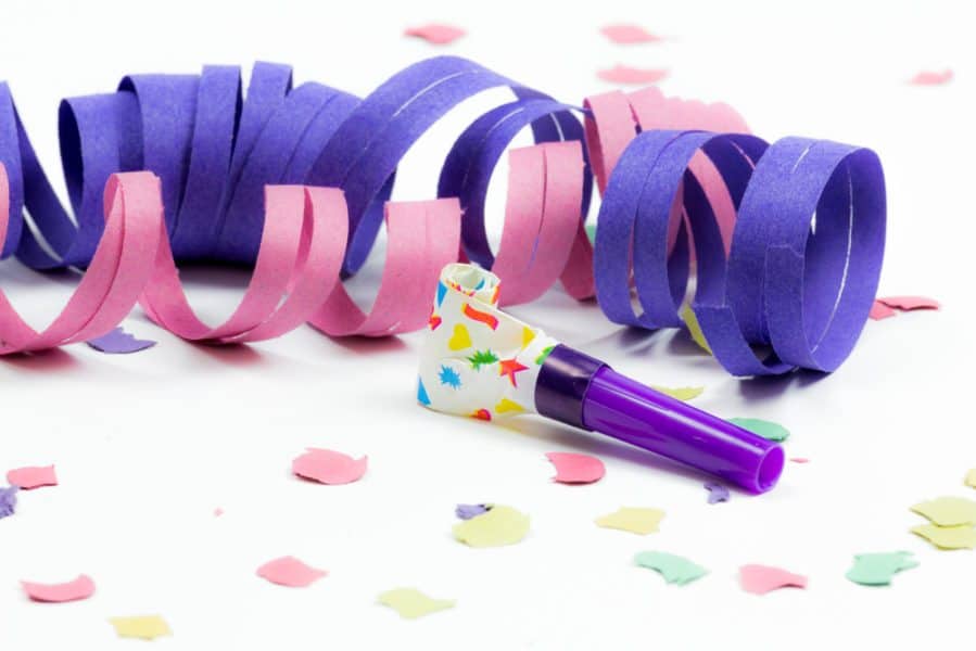photo of colorful streamers, confetti, and noisemaker on white background to celebrate New Year's Eve with kids
