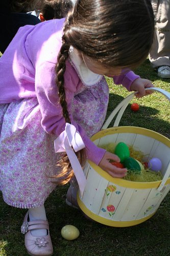 A young girl with a floral dress and pink sweater holding a basket off plastic eggs for an Easter egg hunt