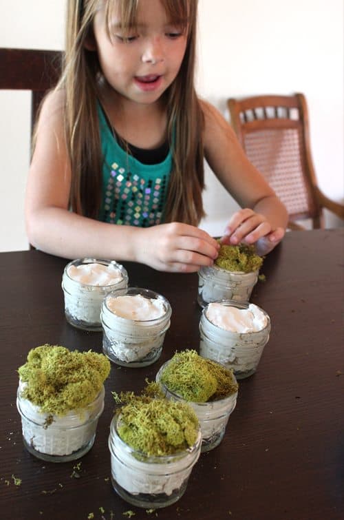 child putting moss and clay in jars for craft 