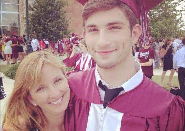 picture of mom and high school son in cap and gown outside of school on graduation day