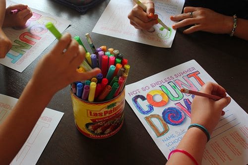 overhead shot of children's hands, coloring summer countdown printables with markers 