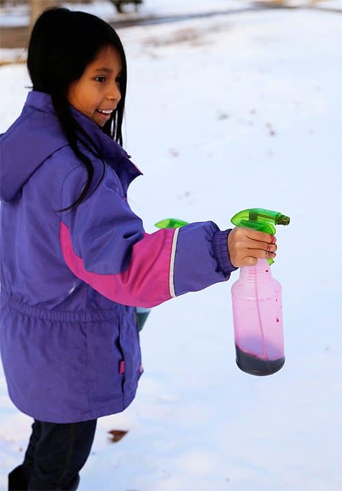 girl squirting spray bottle filled with purple food dye into the snow