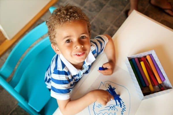 A child sitting in a blue chair, coloring, looking up
