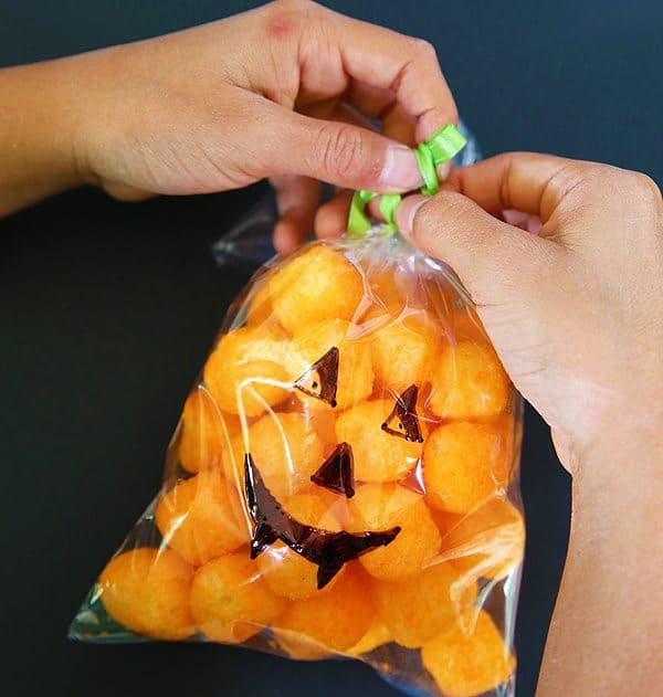 a child's hands tying off a plastic bag filled with cheese puffs with green ribbon