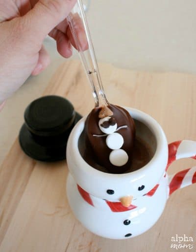 chocolate covered spoon being dipped into a mug filled with hot chocolate 
