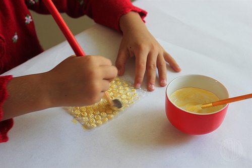 overhead picture of hands painting yellow onto scrap of bubblewrap 