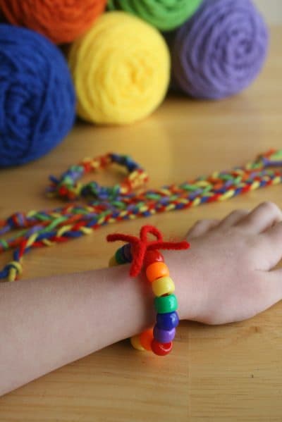 close-up of child's forearm with rainbow beaded bracelet with colorful yarn in background