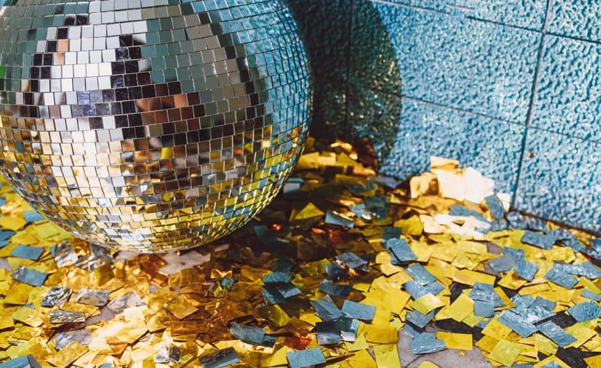 disco ball and silver and gold confetti on the floor resting against a corner