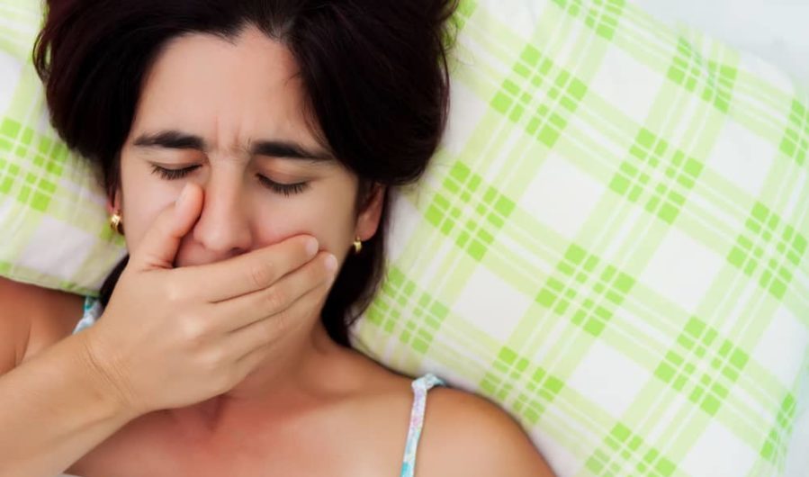 Woman laying in bed and covering her mouth to avoid coughing