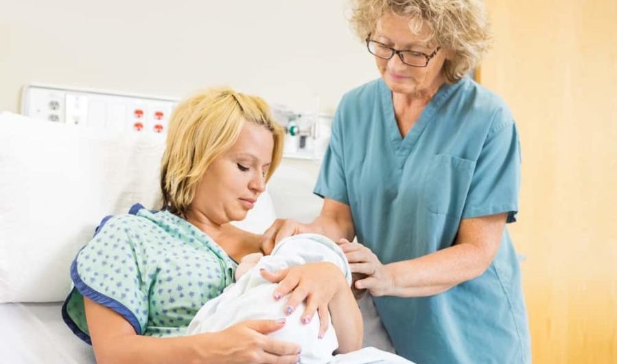 Nurse Assisting Woman In Breast Feeding Baby In Hospital