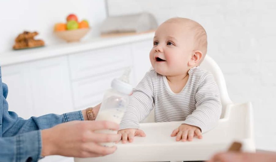 Baby in highchair being fed baby bottle