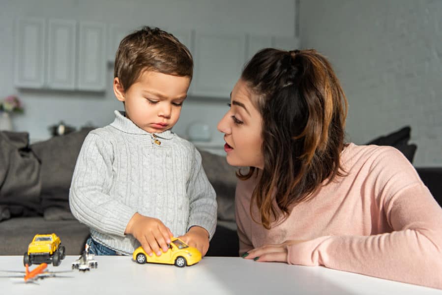 mom talking to little toddler son playing with toy cars at home