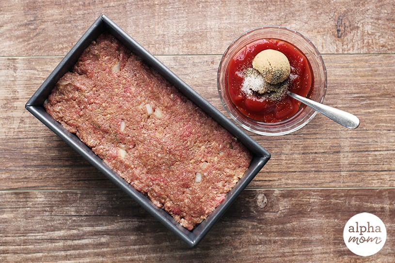 Top view of uncooked meatloaf in a pan with bowl of ketchup-based glaze ingredients on the side