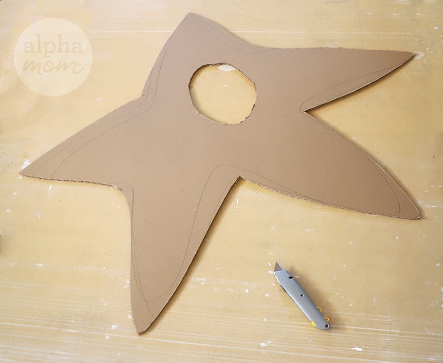 cardboard cut into a star shape with hole in the middle and exacto knife nearby 