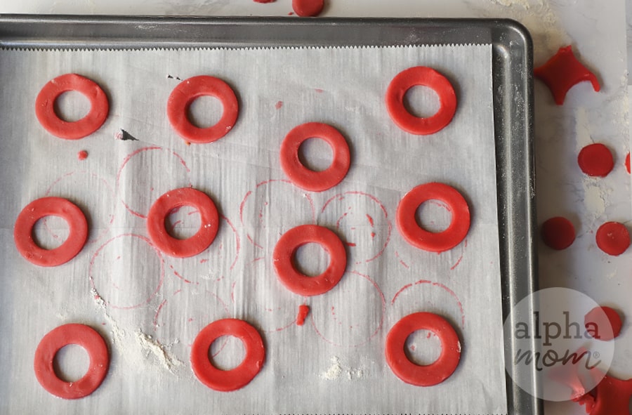 overhead photo of many red O shaped cookie dough on cookie sheet