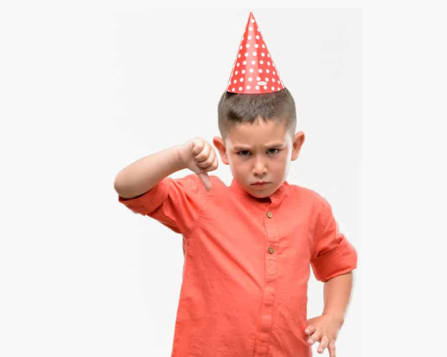 Little boy wearing birthday cap with disappointed face with thumbs down