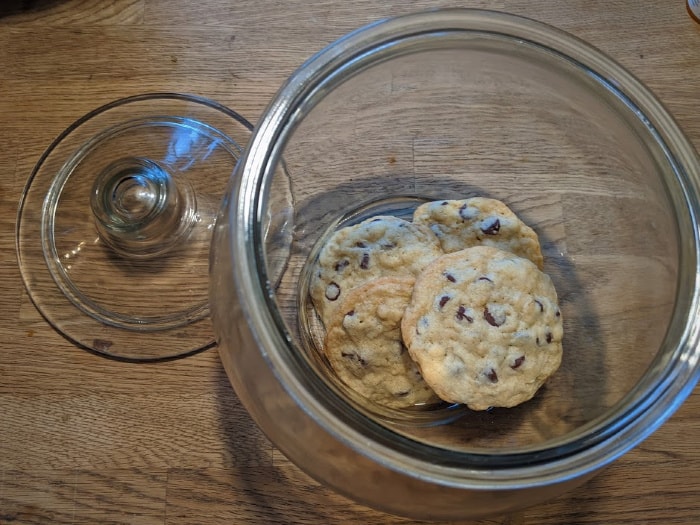 overhead photo of four chocolate chip cookies left at the bottom of a tall glass cookie jar