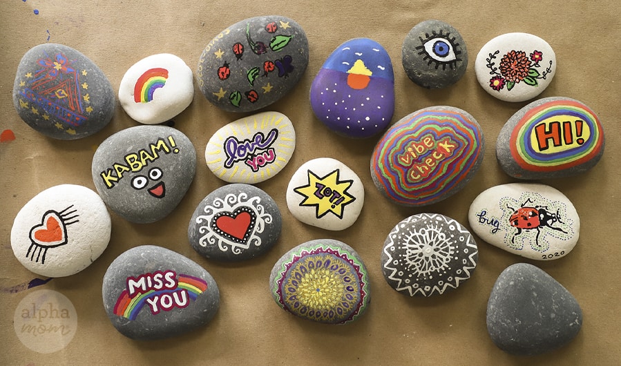 overhead photo of small river rocks painted with kind and inpsiring messages and images