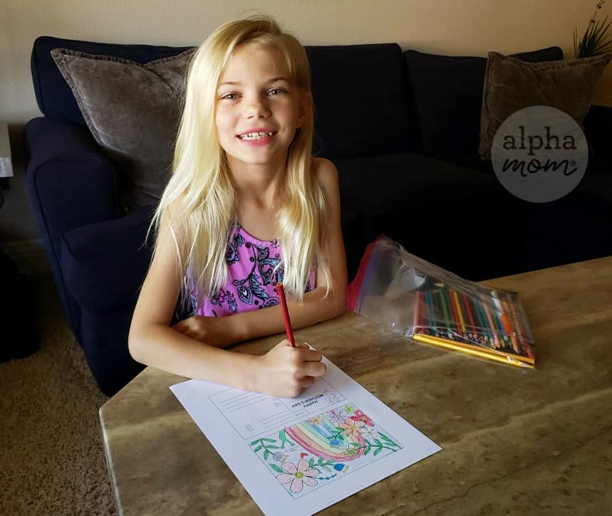 long haired blond girl coloring a postcard at her coffee table with colored pencils