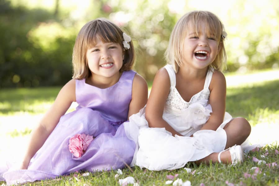 Two young flower girls at a wedding sitting on the grass