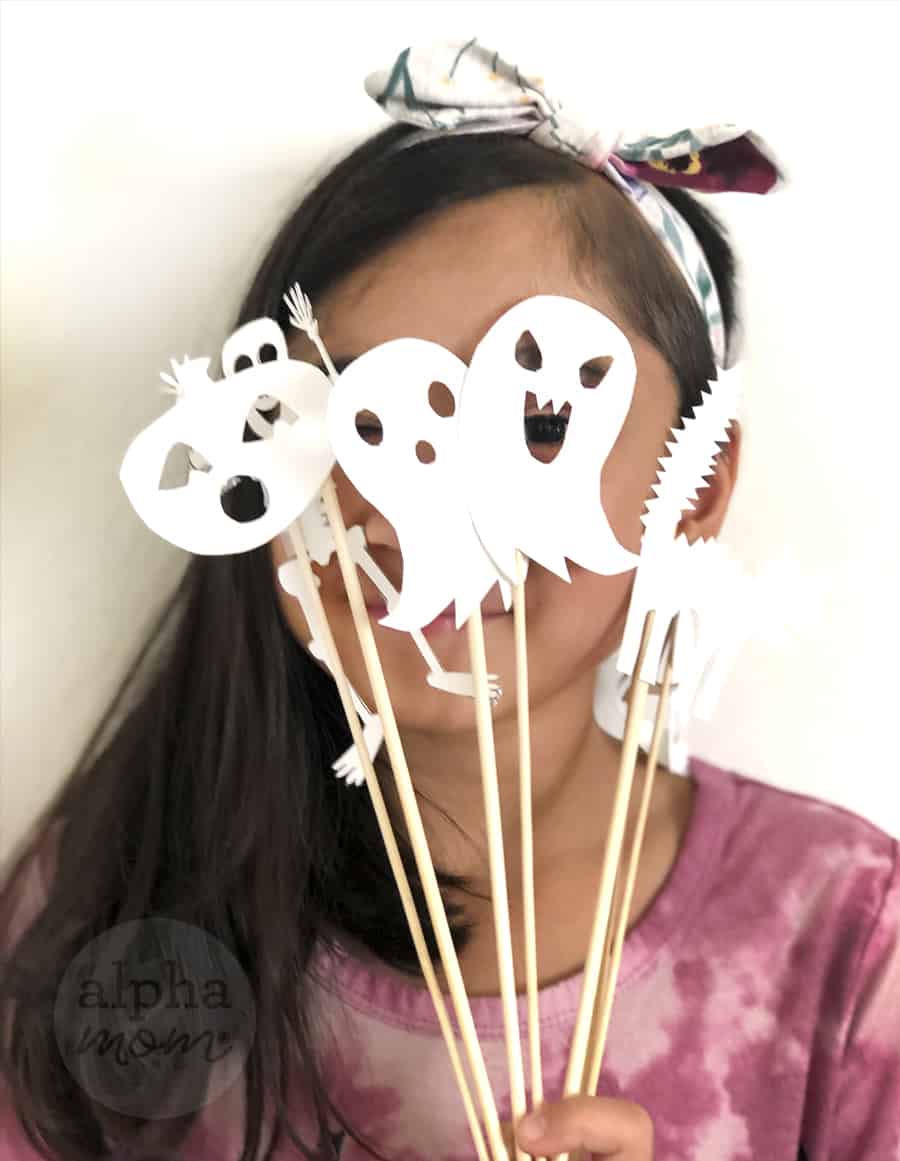 young girl holding up Halloween shadow puppets on sticks in front of her face 