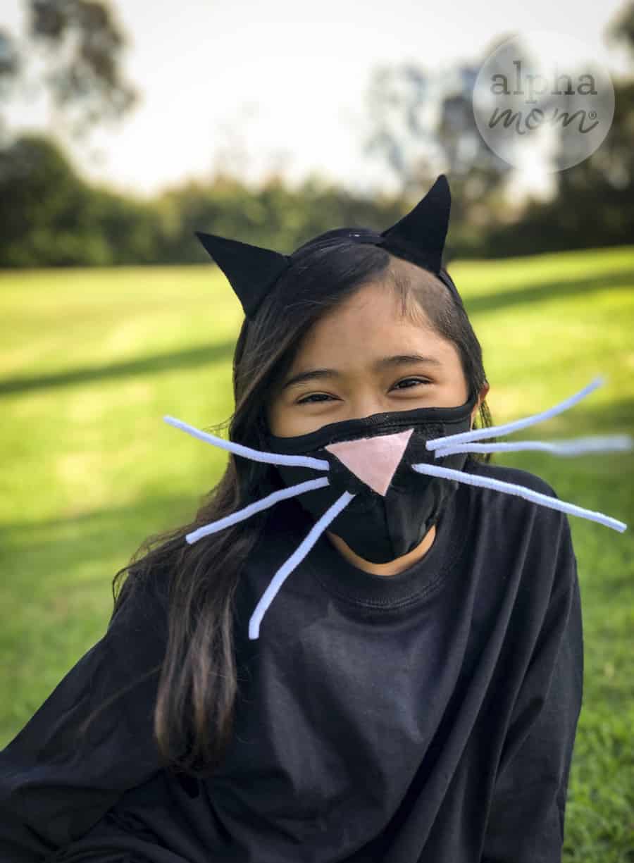 photo of young girl with long black hair wearing homemade cat face mask and ears on headband for Halloween costume during COVID 