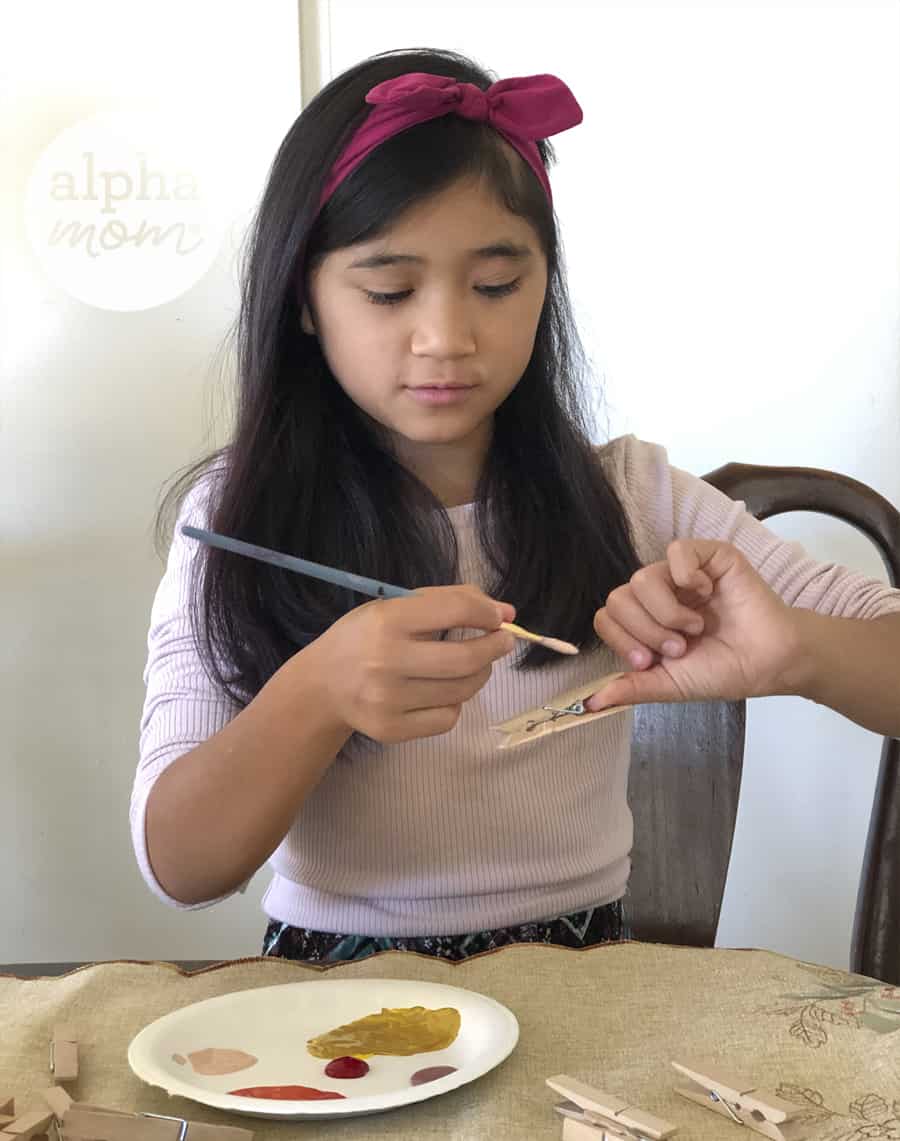 photo of girl painting clothespin with paintbrush 