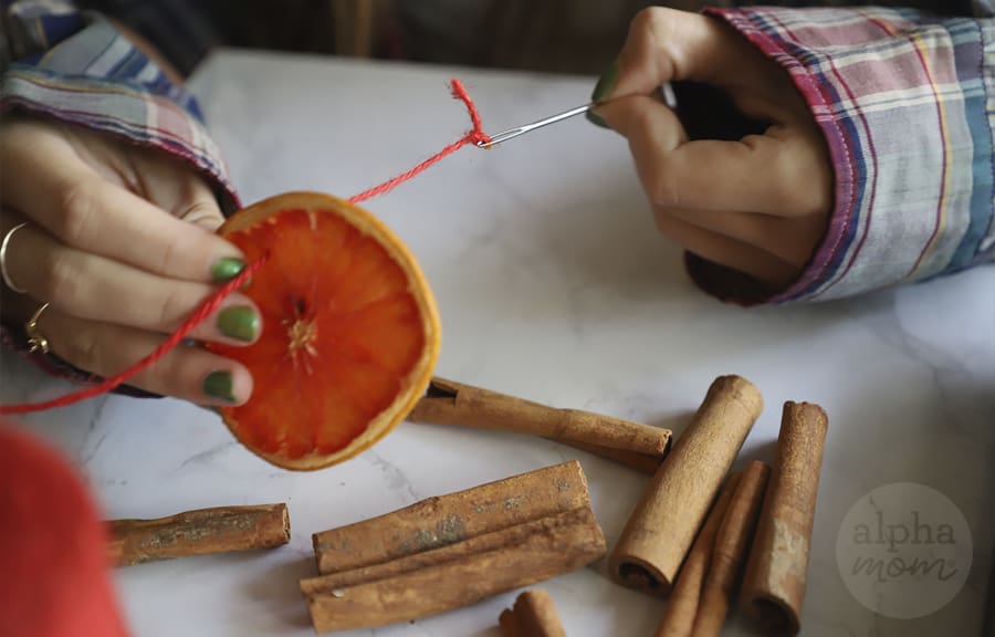 close-up of girl pulling sewing needle through a baked pink grapefruit slice