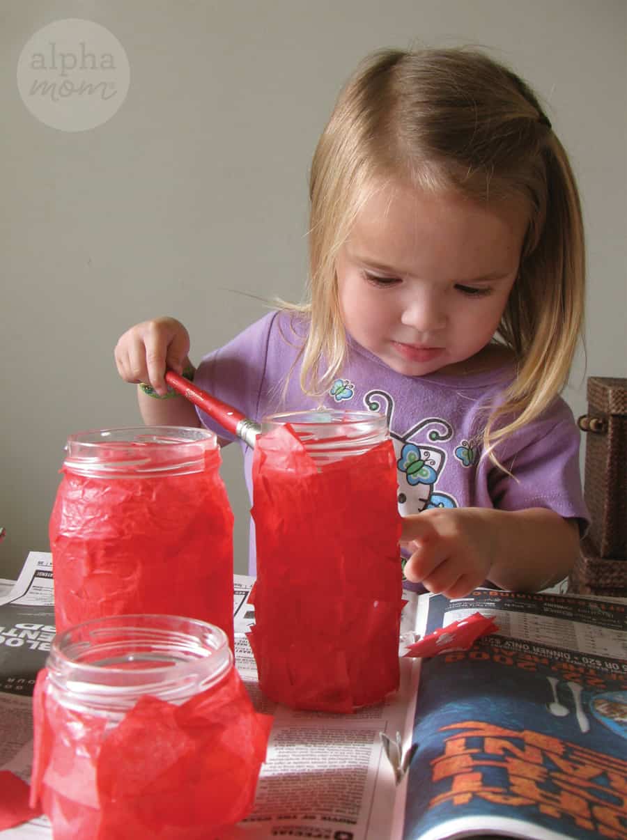little blond girl decoupaging glass jars with red tissue paper 
