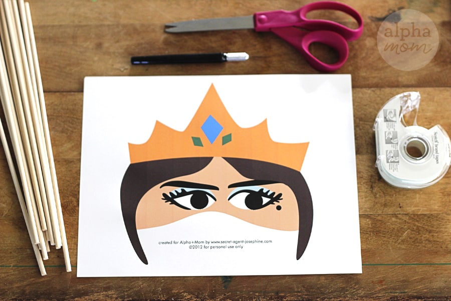 overhead photo of supplies to make Queen Esther face mask for Purim. Photo of printable, scissors, tape, holding stick, xacto knife