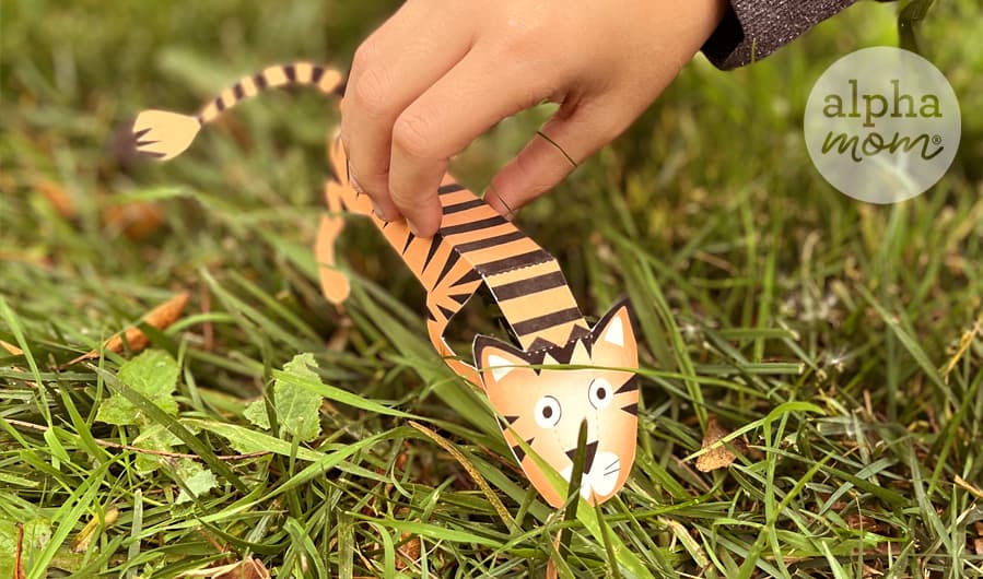 picture of a homemade paper tiger toy being held and played with in the grass with a child's hand in close-up