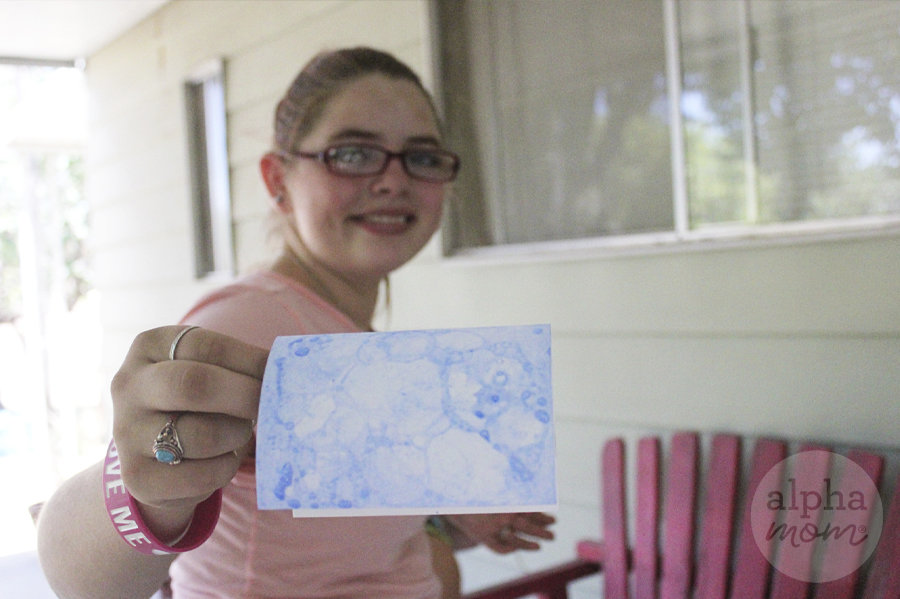 teen girl with glasses holding up cardstock with blue bubble art on paper