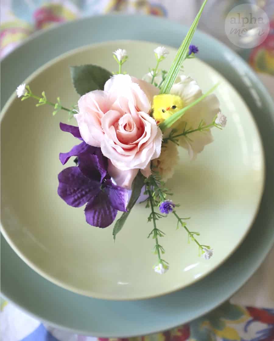 overhead photo of tiny vase filled with fake flowers used as name place card on table setting of mint green soup bowl and duck egg blue plate