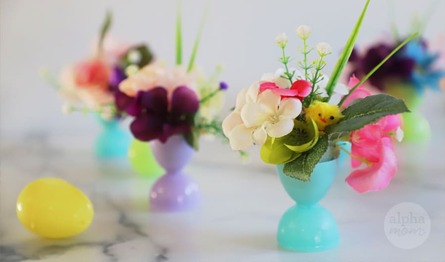 four mini bouquets of faux flowers arranged in plastic Easter eggs that have been glued together on top of marble table