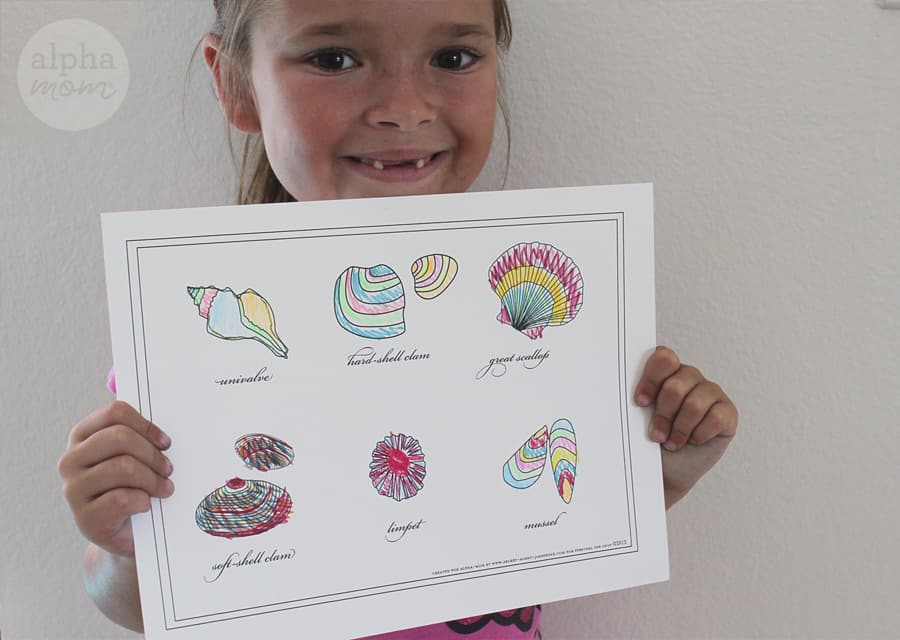 little smiling blond girl with hair in a pony tail and missing two front teeth holding up a colored in sea shell printable in very colorful hues