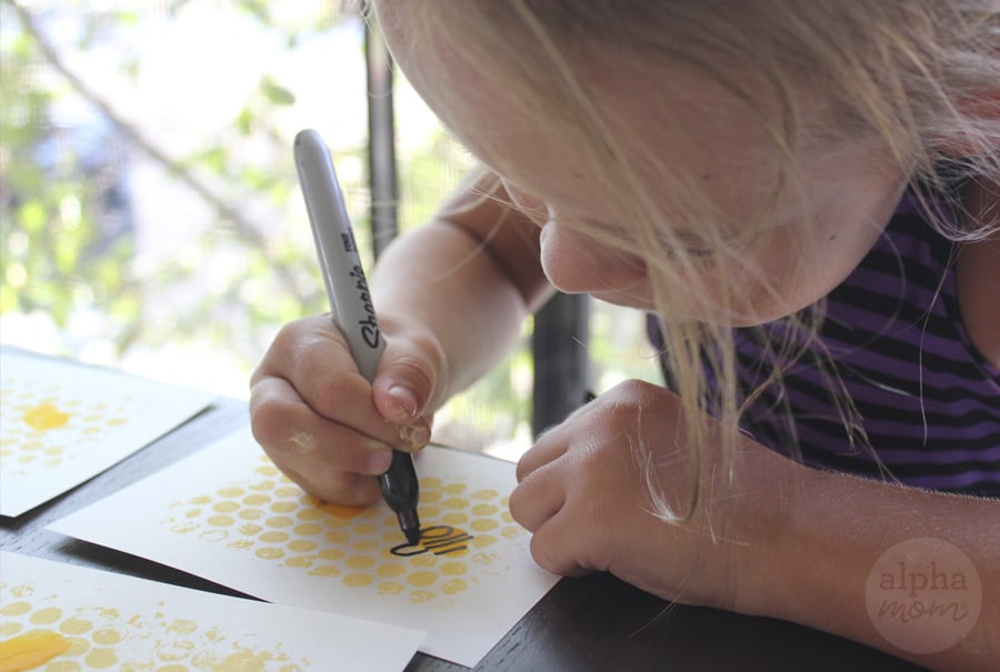 Little girl drawing bee with black sharpie onto cardstock with yellow-painted bubblewrap to make Rosh Hashanah Honey Bee Cards